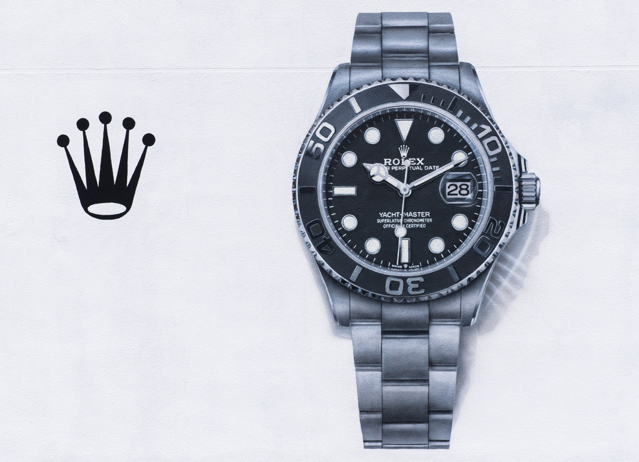 Minimalistische Darstellung der Rolex Yacht-Master und Krone als zentrales Element auf weißer Wandfläche.