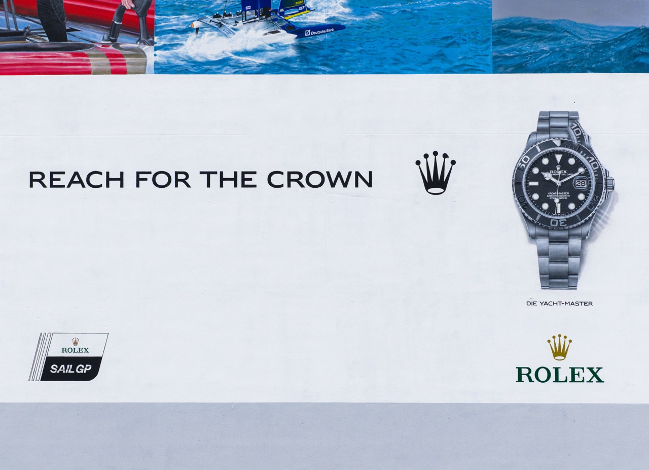 Unterer Bereich des Murals mit Claim „Reach for the Crown“, Rolex Logo und Abbildung der Yacht-Master Uhr.