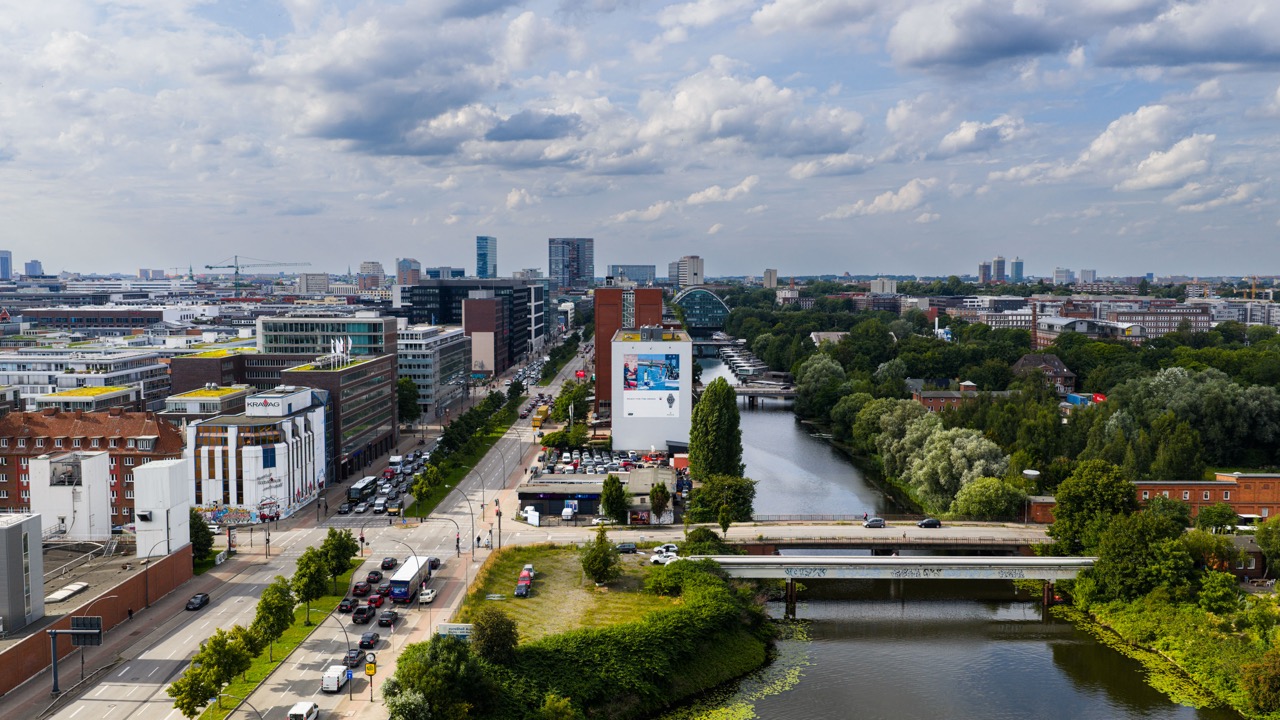 Luftaufnahme von Hamburg mit Blick auf das großformatige Rolex SailGP Mural an einer Gebäudefassade entlang eines Kanals.