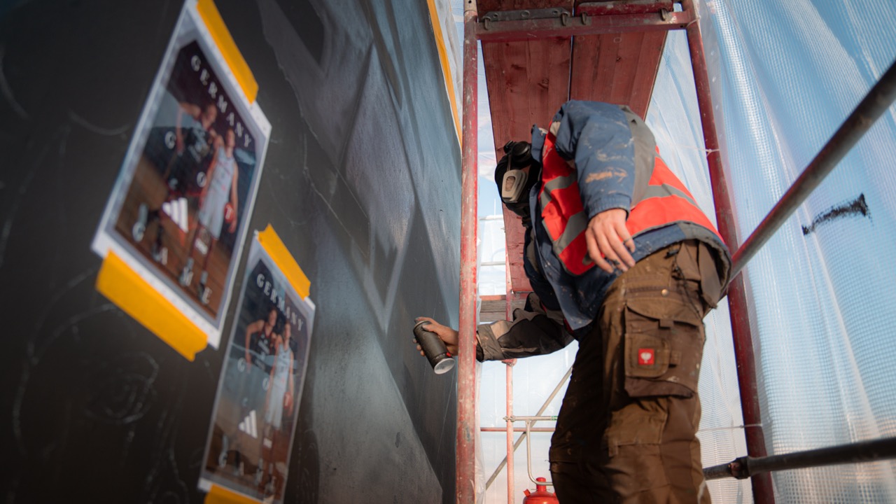 Künstler arbeitet auf dem Gerüst an den ersten großflächigen Bereichen des adidas Basketball-Murals in Berlin.
