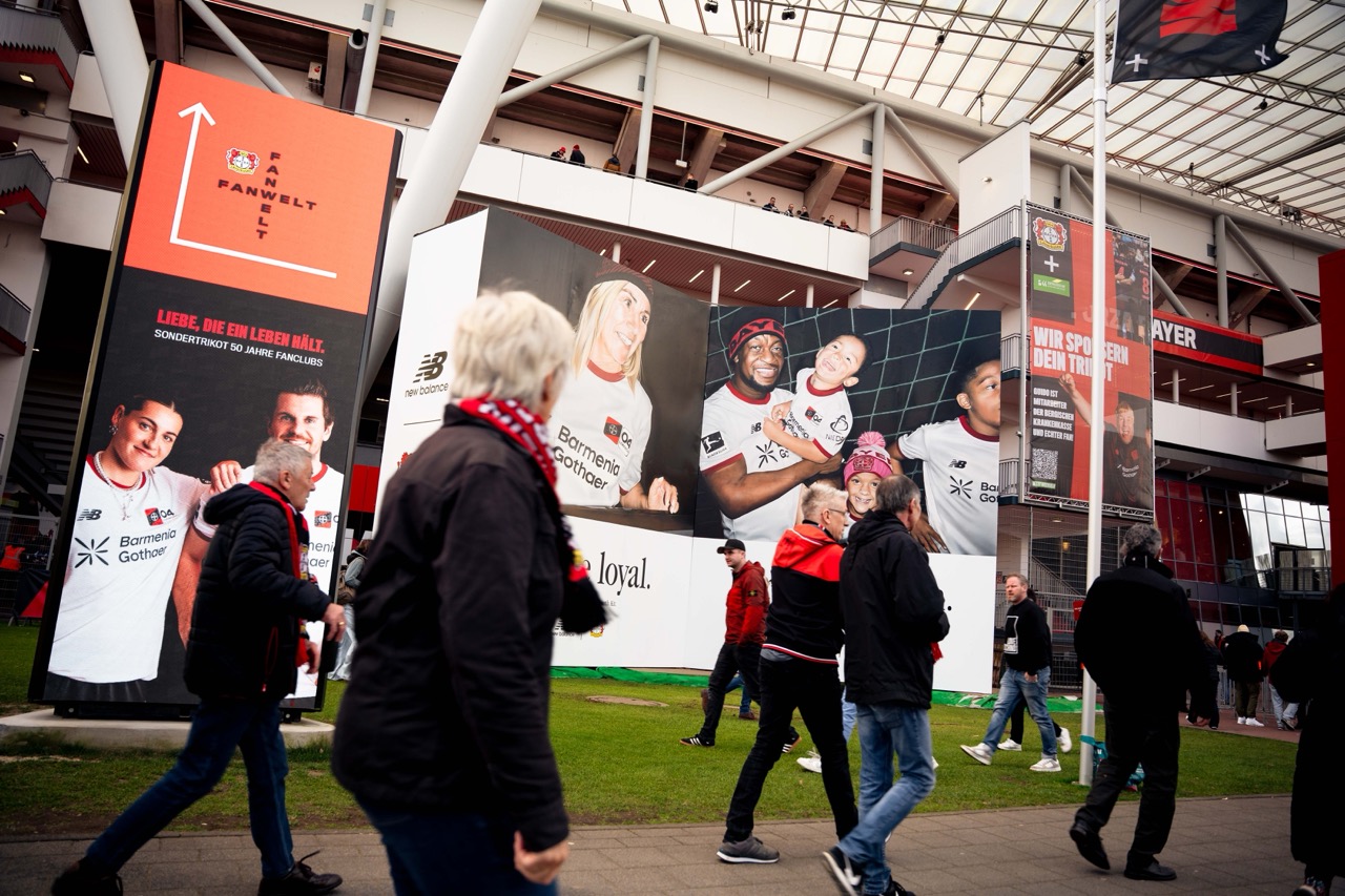 Fertige Muralinstallation von New Balance und Bayer 04 Leverkusen vor dem Stadion mit vorbeilaufenden Fans am Spieltag.