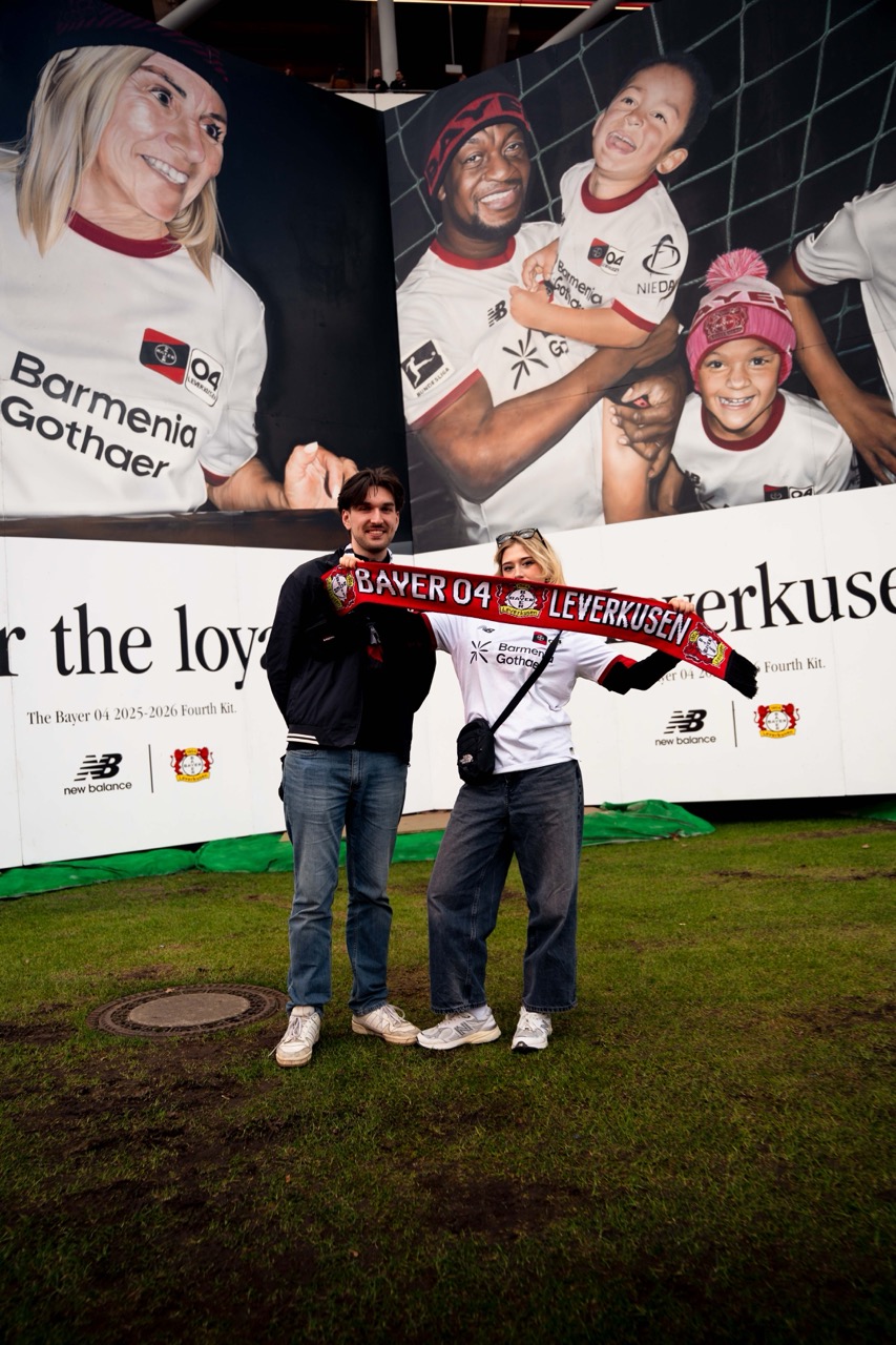 Zwei Fans posieren mit Bayer-04-Schal vor der großformatigen Installation des neuen Sondertrikots.