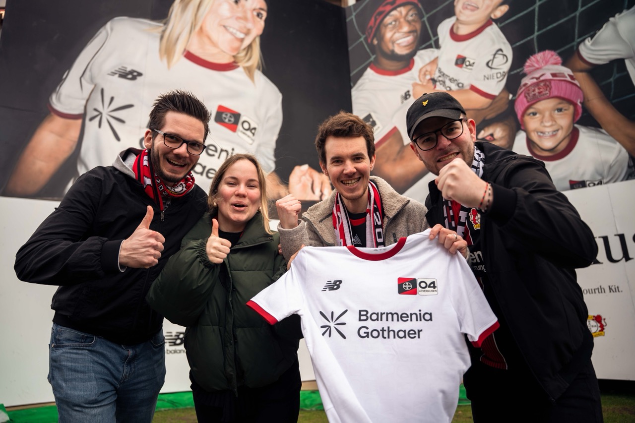 Gruppe von Bayer-04-Fans präsentiert das neue Trikot vor der großformatigen Muralinstallation.