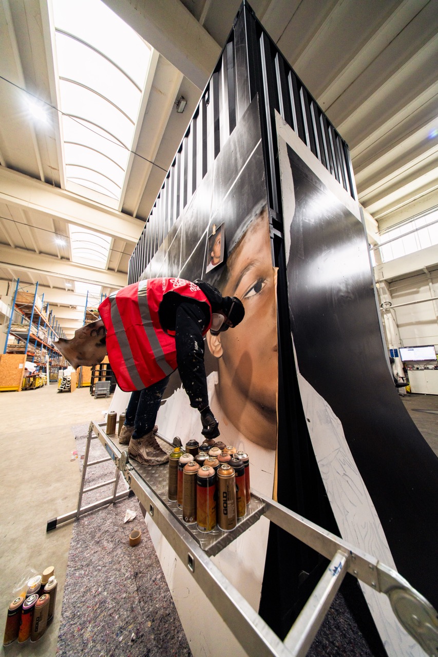 Künstler bei der Arbeit an einem großformatigen Muralmodul im Studio. Mit Sprühdose und Referenzbild entsteht ein fotorealistisches Portrait auf einzelnen Installationselementen.