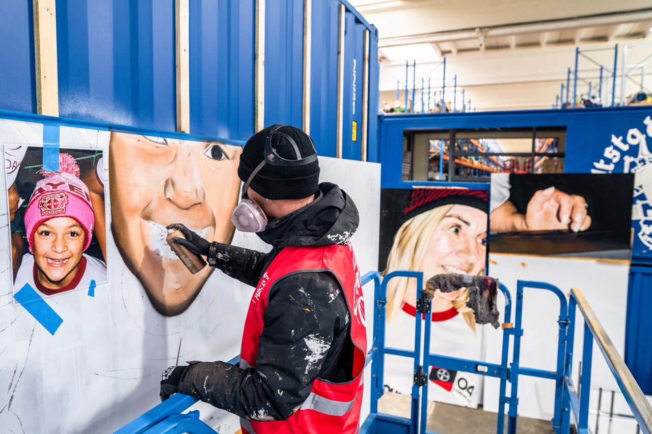 Künstler bei der Ausarbeitung eines Portraits auf einem großformatigen Muralmodul innerhalb der Produktionshalle.