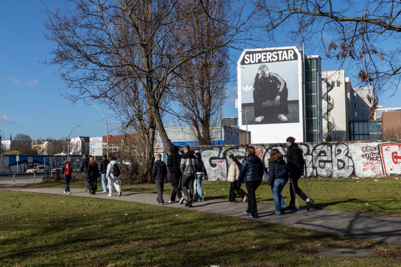 adidas Superstar Mural mit Lamine Yamal an einer Berliner Hausfassade, aufgenommen hinter einer Gruppe vorbeilaufender Menschen.