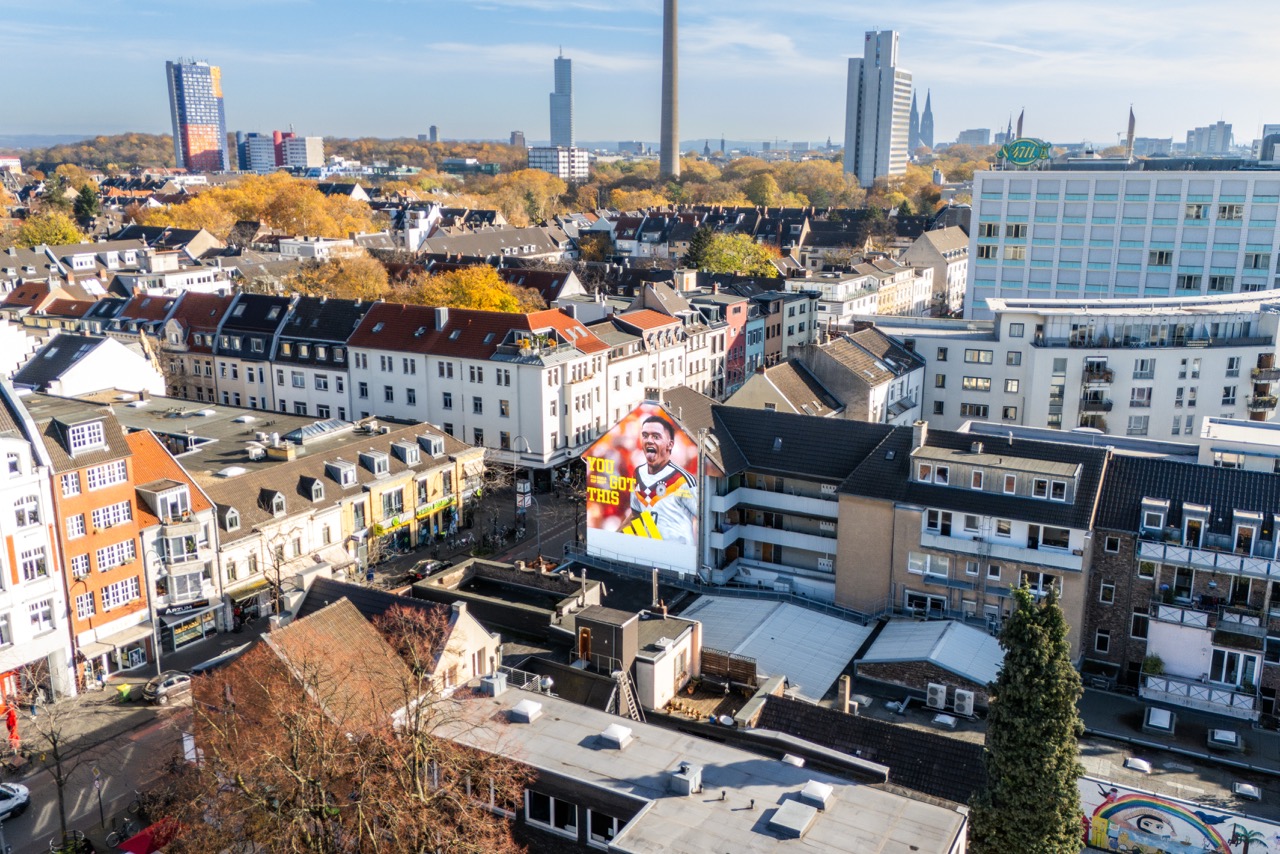 Weite Drohnenaufnahme des DFB Murals von Florian Wirtz zwischen den Häusern und Straßen von Köln-Ehrenfeld.