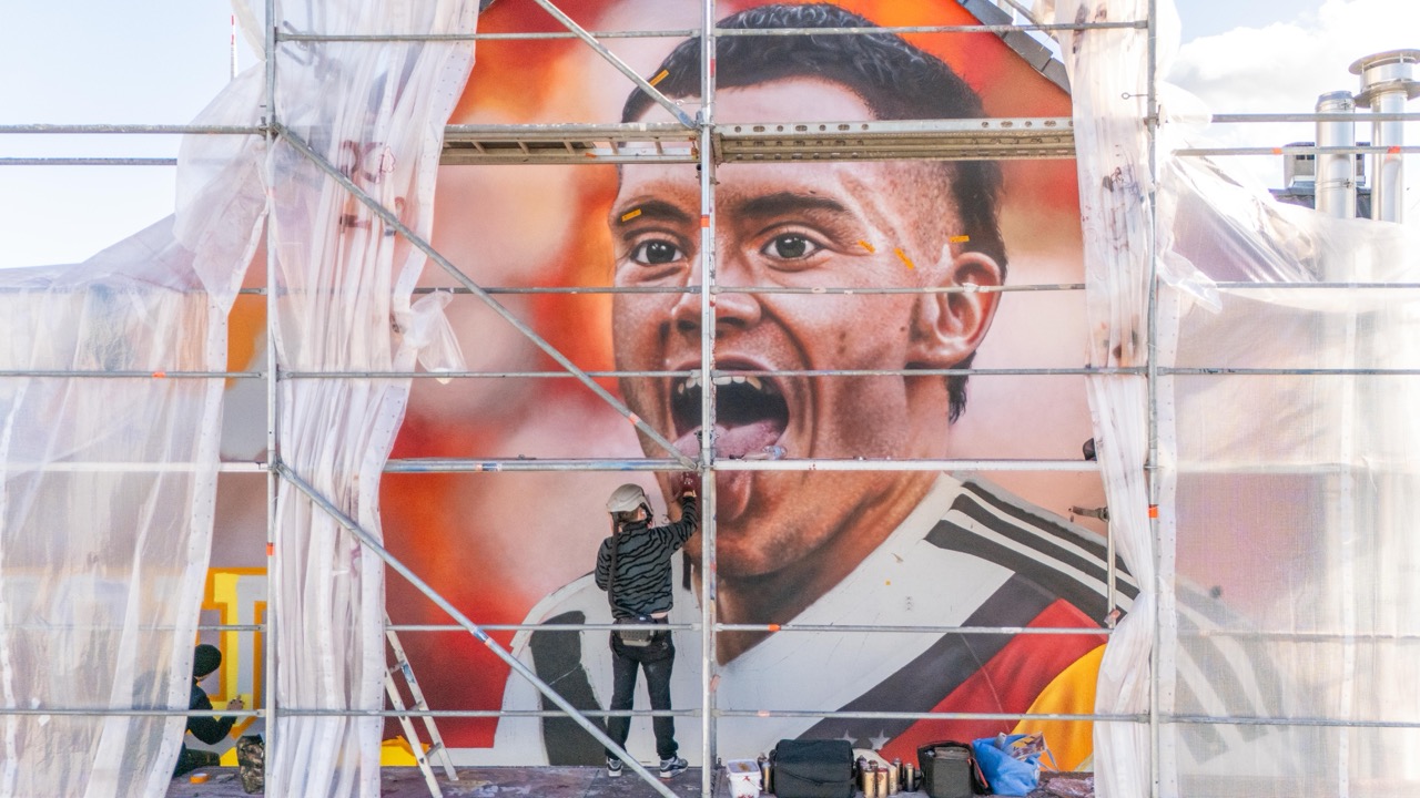 Artist arbeitet auf einem großformatigen Florian-Wirtz-Mural auf einem Gerüst in Köln-Ehrenfeld, während das neue DFB Heimtrikot als riesiges Wandbild entsteht.