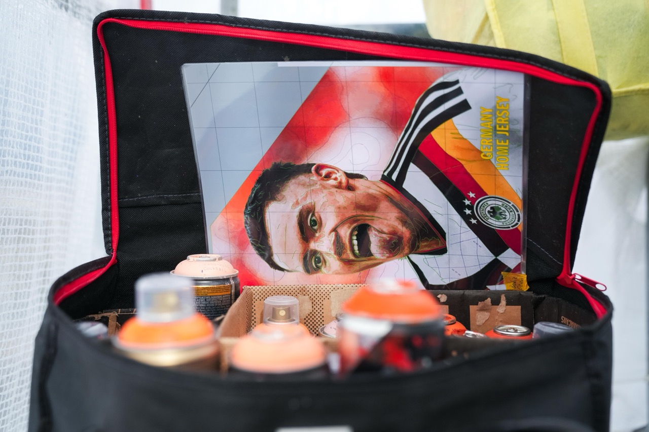 Vorlage des Florian-Wirtz-Artworks für das DFB Heimtrikot liegt zwischen Spraydosen und Arbeitsmaterial auf dem Gerüst des Murals.
