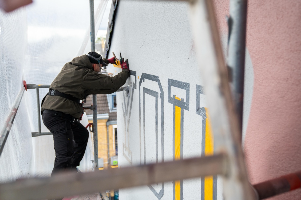 Artist arbeitet auf dem Gerüst an typografischen Elementen des DFB Murals neben dem großformatigen Portrait von Florian Wirtz.