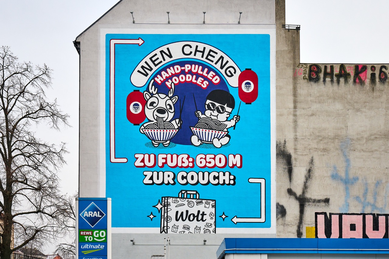 Detailansicht des WOLT-Murals an einer Giebelwand mit Wen Cheng Noodles Motiv, roten Lampions und auffälligem türkisfarbenem Hintergrund.