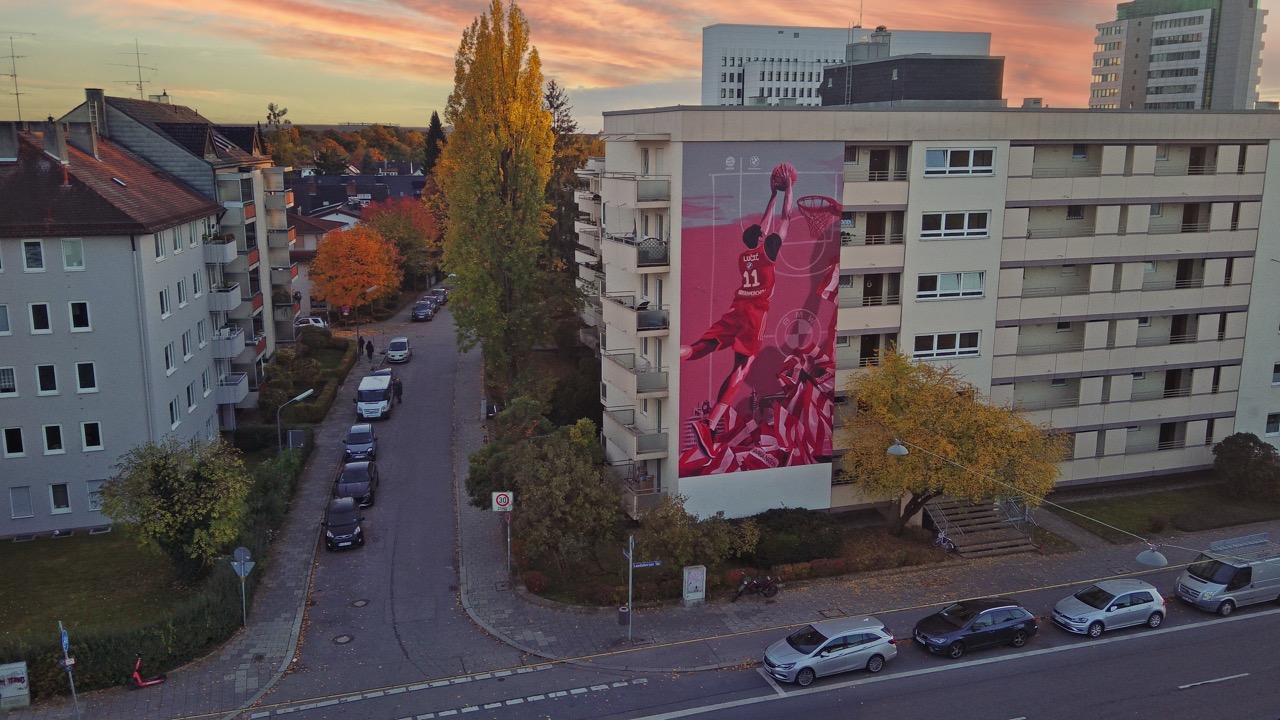 Drohnenaufnahme des FC Bayern Basketball Murals zwischen Wohnhäusern und herbstlichen Straßen in München.