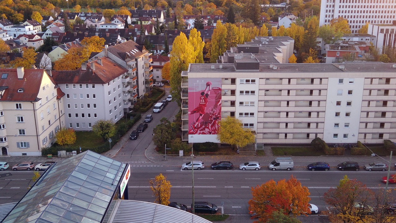 Luftaufnahme des FC Bayern Basketball Murals an einer Münchner Gebäudefassade mit Blick auf die umliegende Stadtlandschaft.