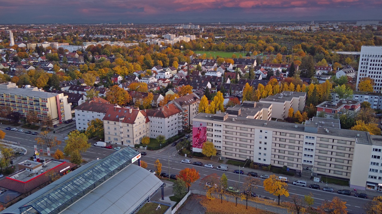 Drohnenaufnahme eines großformatigen FC Bayern Basketball Murals an einer Wohnhausfassade in München bei herbstlicher Abendstimmung.