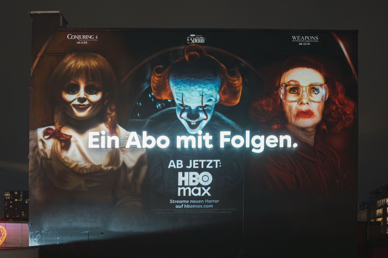 Nächtliche Frontansicht des HBO-Max-Murals mit leuchtendem 3D-Claim „Ein Abo mit Folgen“ und bekannten Horrorfiguren.
