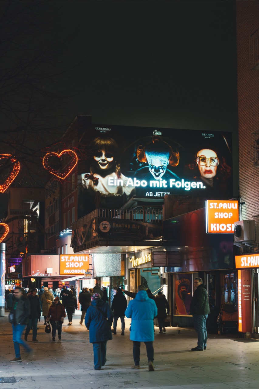 HBO-Max-Mural mit leuchtendem Kampagnenclaim über einer belebten Straße auf St. Pauli bei Nacht.