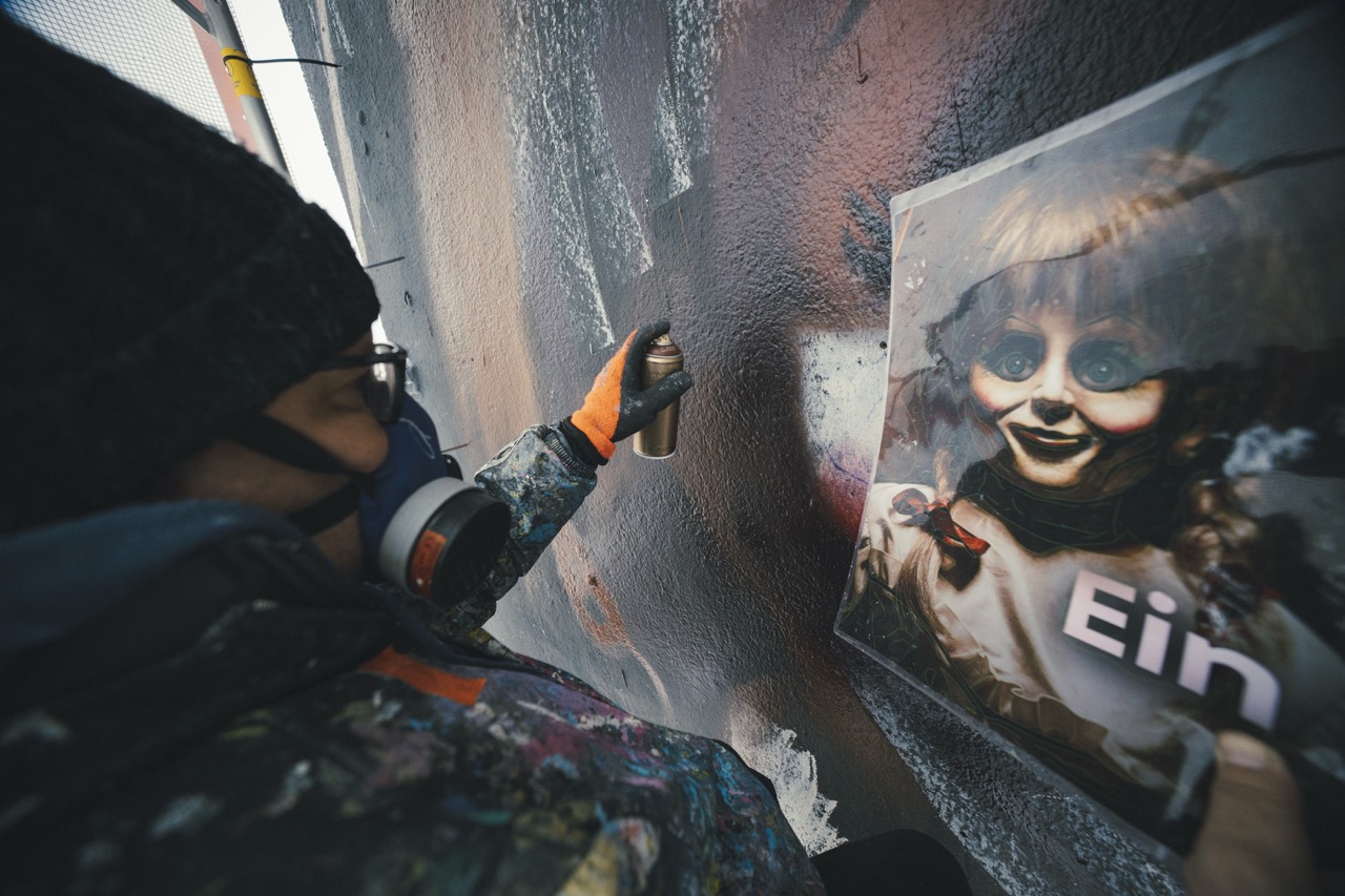 Künstler sprüht die ersten Flächen des HBO-Max-Murals anhand einer Motivvorlage auf die vorbereitete Fassadenwand.