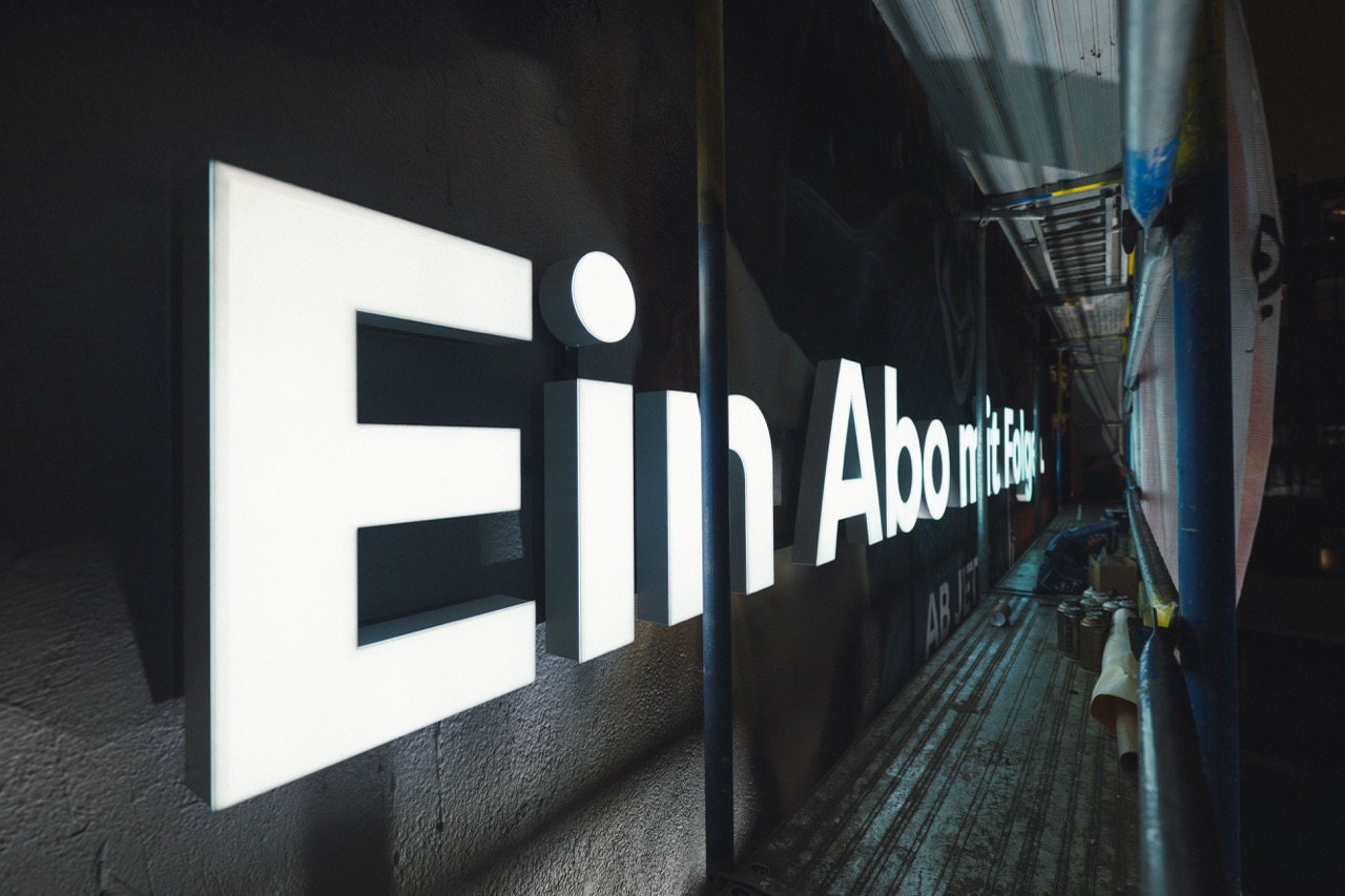 Leuchtende weiße 3D-Buchstaben des Slogans „Ein Abo mit Folgen“ auf der Fassade während der Installation bei Nacht.