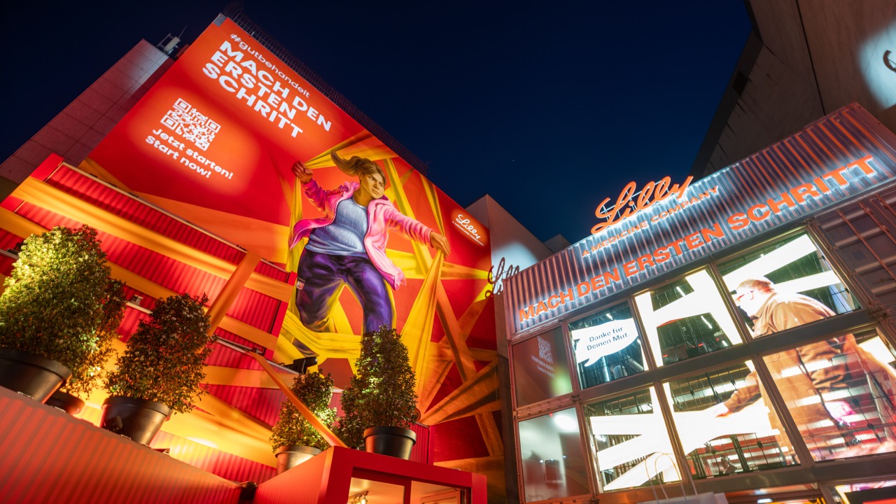Großformatiges Lilly Mural und beleuchtete Markeninstallation am Berliner Ku’damm während der Abendstunden.