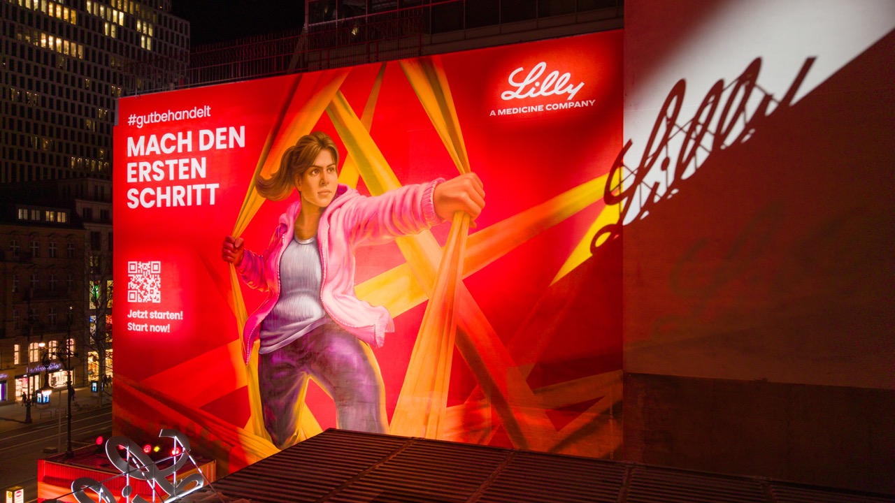 Detailaufnahme des beleuchteten Lilly Murals mit figurativer Illustration und grafischer Fassadengestaltung.