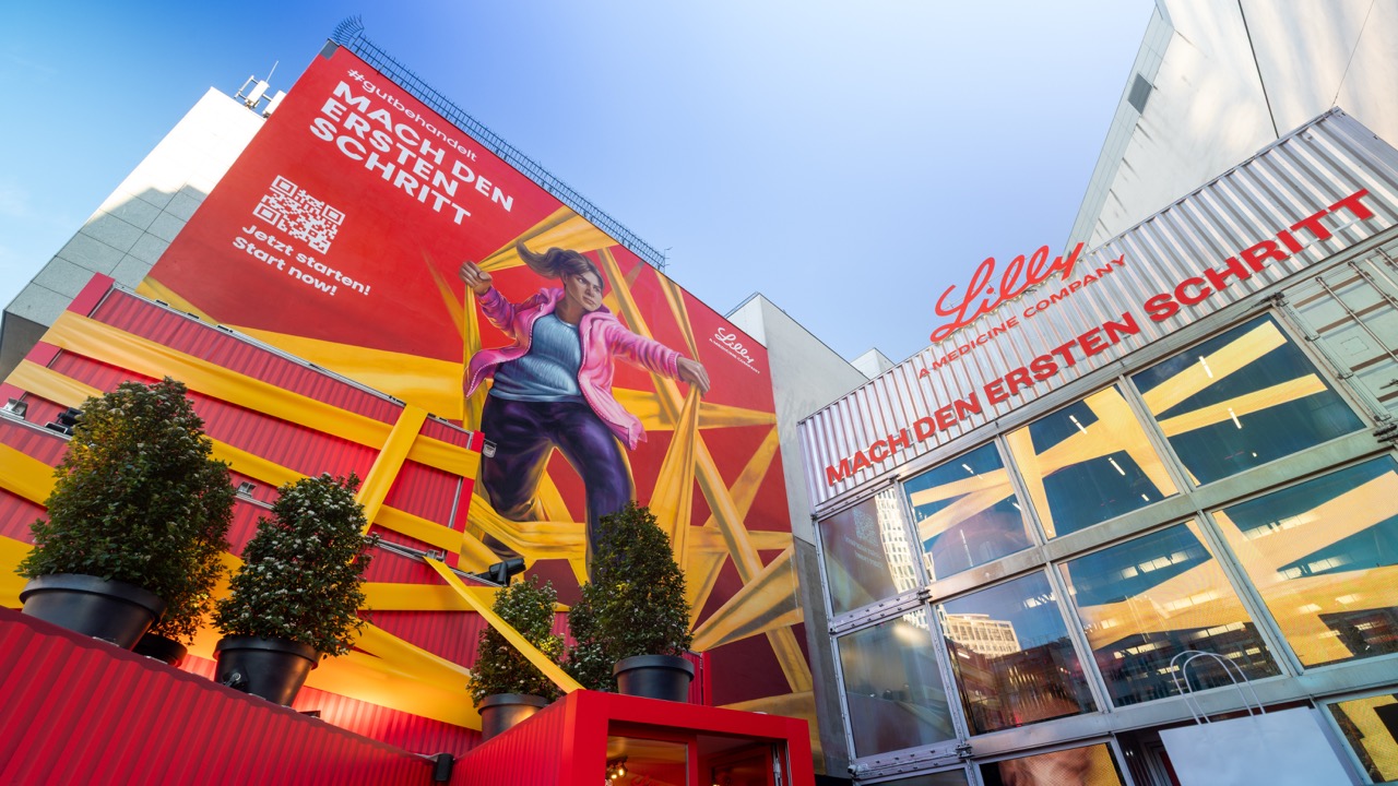 Perspektivische Aufnahme des großformatigen Lilly Murals am ehemaligen The Space am Berliner Ku’damm mit ergänzender Markeninstallation und leuchtenden Rot- und Gelbtönen.