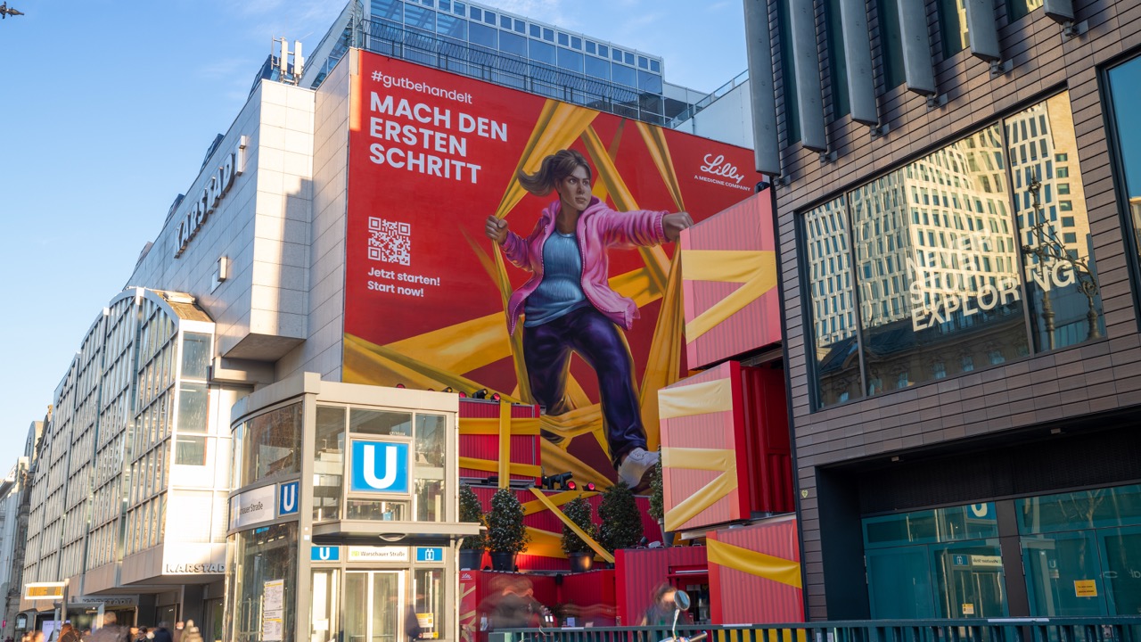 Großformatiges Fassadenmural für Lilly am Berliner Ku’damm mit Blick auf den U-Bahn-Zugang und die umliegende Architektur.