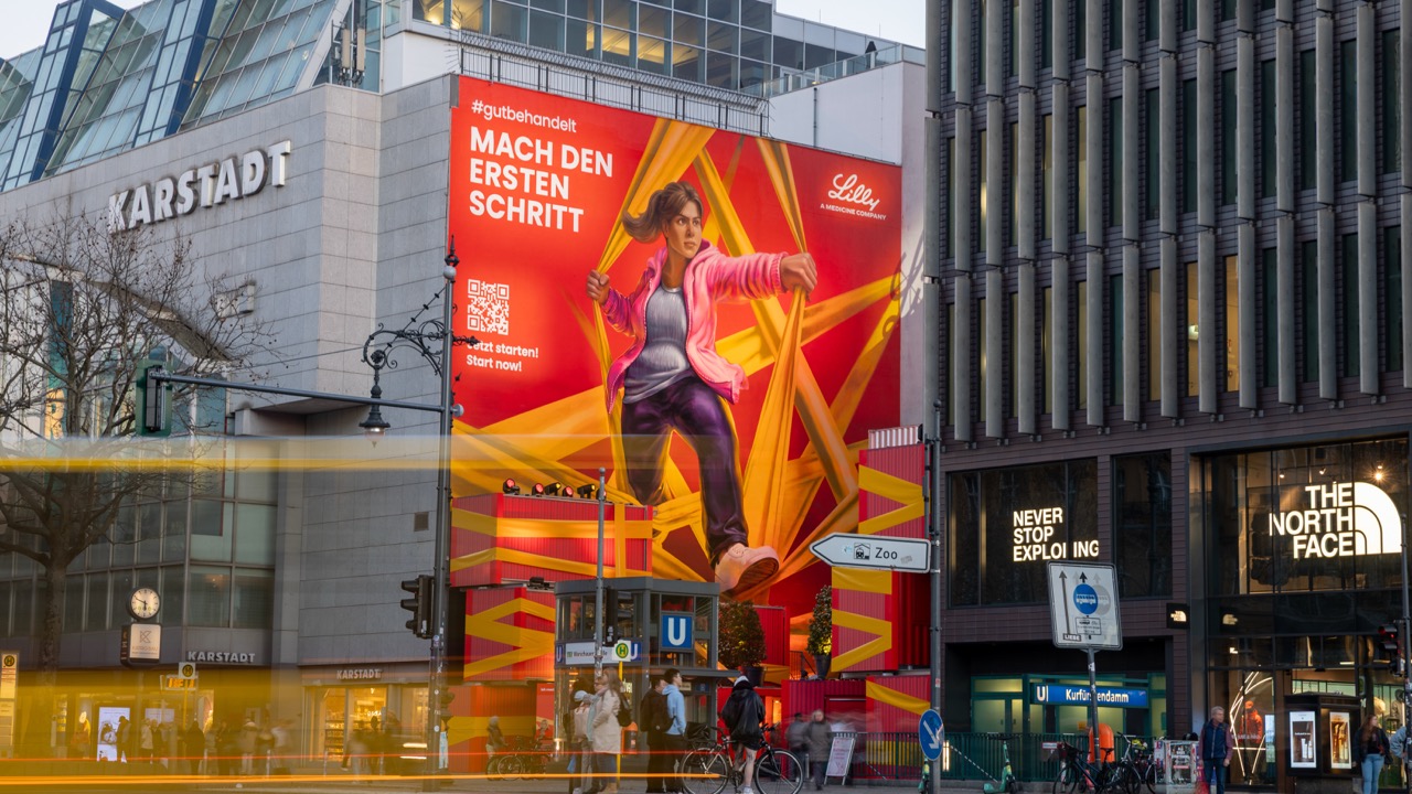 Lilly Mural und Markeninstallation am Berliner Ku’damm während der blauen Stunde mit leuchtender Fassadenbeleuchtung.