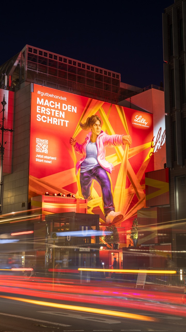 Großformatiges Mural für Lilly am ehemaligen Masumi Space („The Space“) am Berliner Ku’damm bei Nacht. Das Artwork zeigt eine dynamische Figur, die durch leuchtende Formen nach vorn tritt, während das Gebäude im Rahmen eines kompletten Fassaden-Takeovers in kräftigen Rot- und Orangetönen inszeniert wurde.