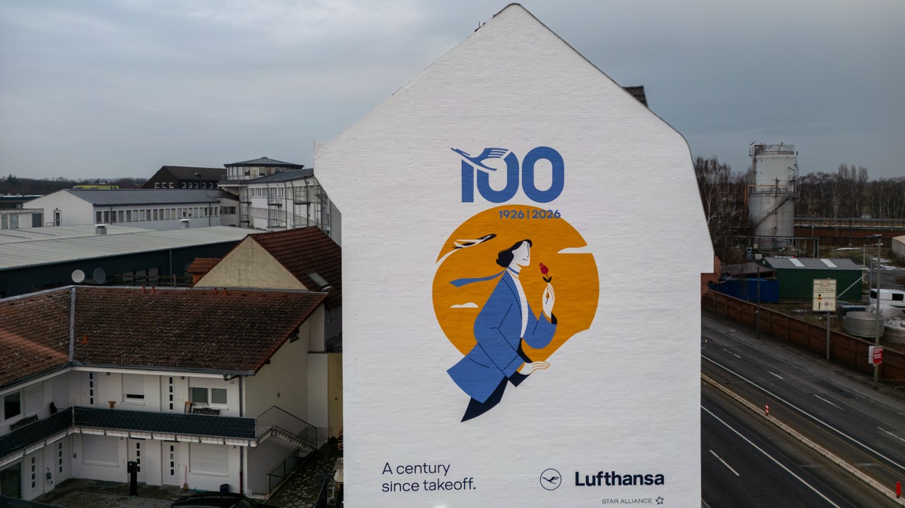 Drohnenaufnahme eines minimalistischen Lufthansa-Murals an einer weißen Hausfassade in Frankfurt am Main.
