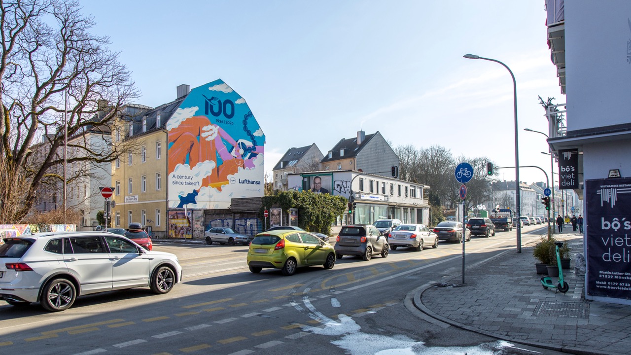 Lufthansa-Mural an einer großen Hausfassade in München bei Tageslicht entlang einer vielbefahrenen Straße.