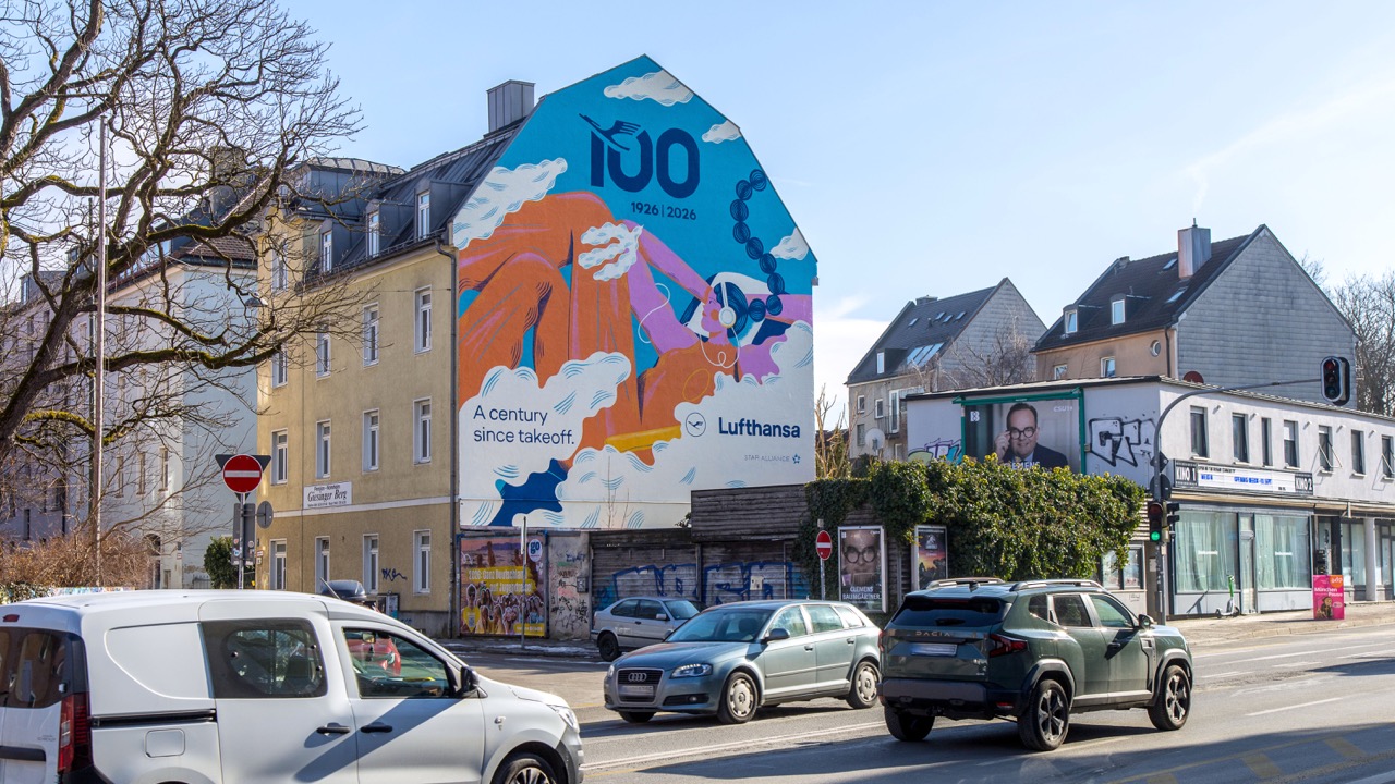 Detailansicht eines großformatigen Lufthansa Jubiläums-Murals mit vorbeifahrenden Autos im Vordergrund.