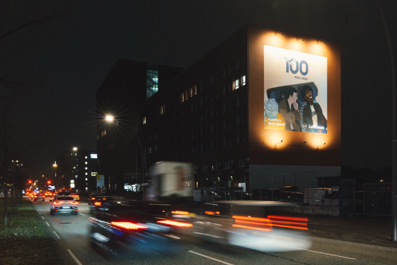 Großformatiges beleuchtetes Lufthansa-Mural an einer stark befahrenen Straße in Hamburg bei Nacht.