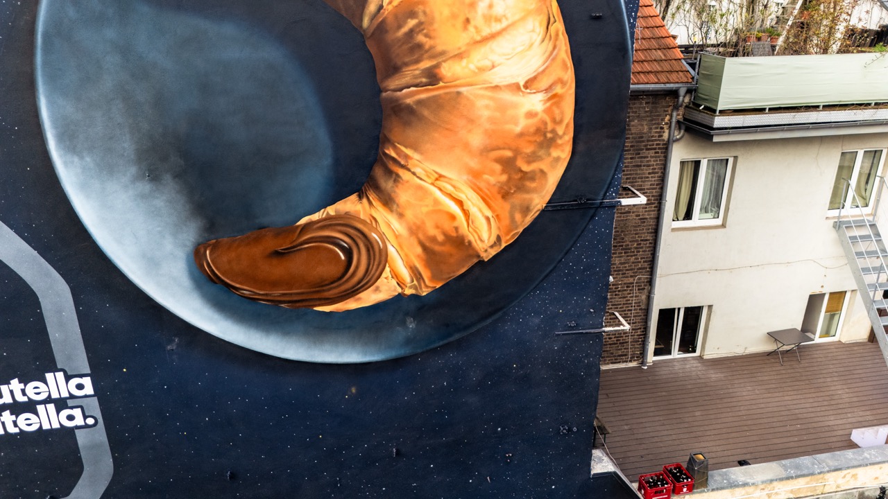 Detailaufnahme des handgemalten Croissant-Motivs mit Nutella-Füllung vor kosmischem Hintergrund.