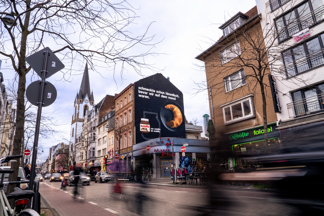 Straßenansicht des fertigen Nutella MOTION MURAL® in Köln mit Bewegungsunschärfe der Passant*innen.