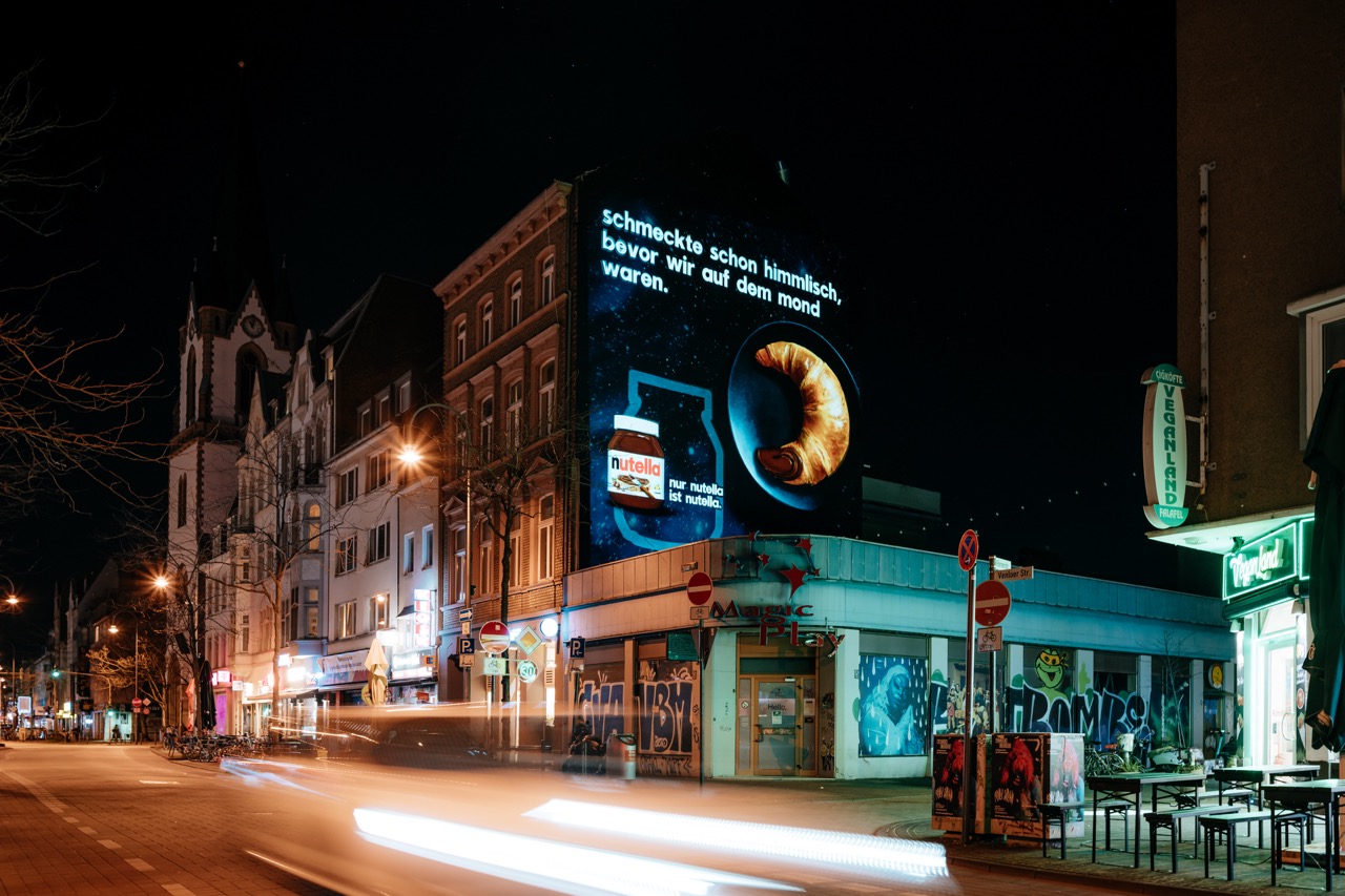 Nachtaufnahme des beleuchteten Nutella MOTION MURAL® in Köln mit Lichtspuren im Vordergrund.