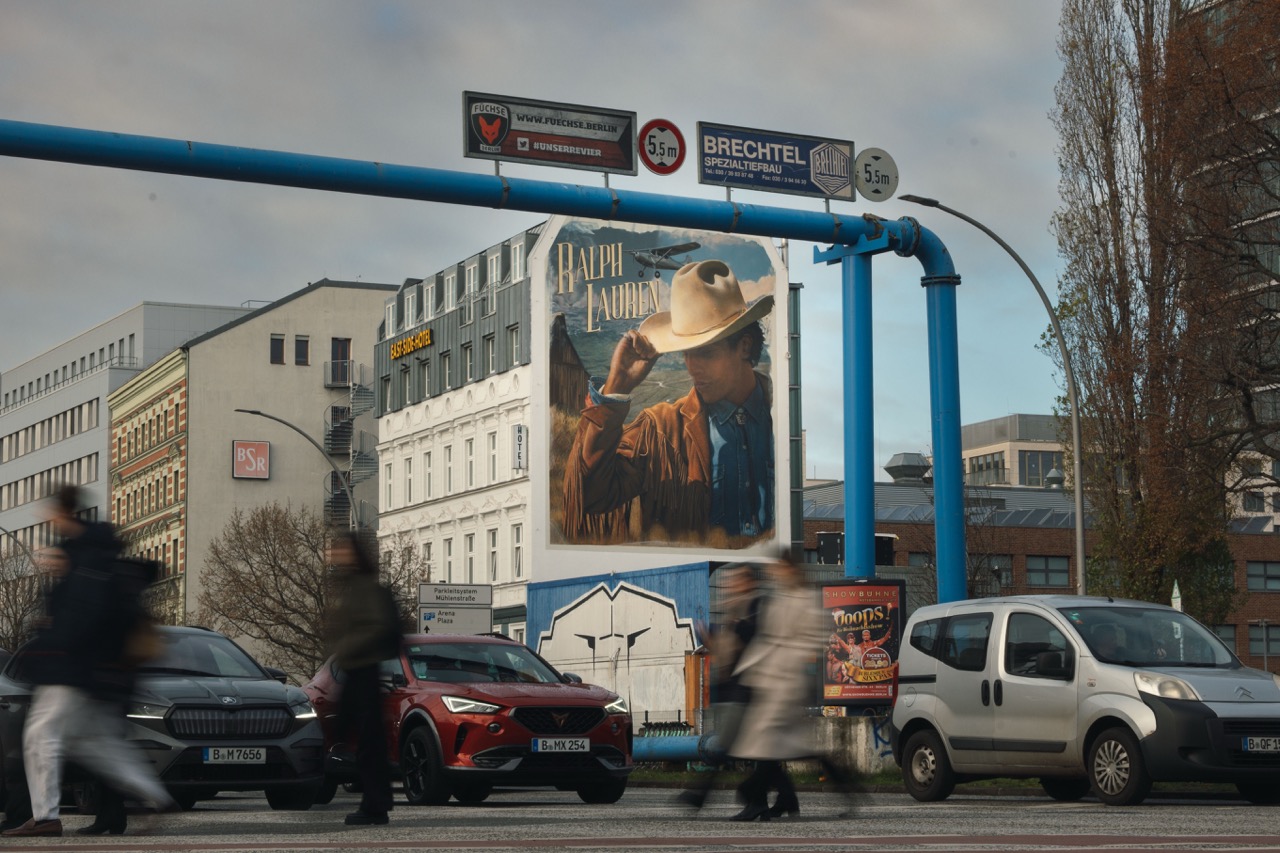Beleuchtetes Ralph-Lauren-Mural bei Nacht mit vorbeiziehenden Lichtspuren des Berliner Verkehrs.