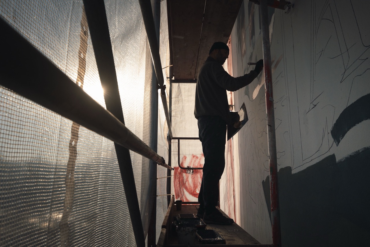 Silhouette eines Artists auf engem Gerüst während der Vorzeichnung eines großformatigen Murals für Ralph Lauren.