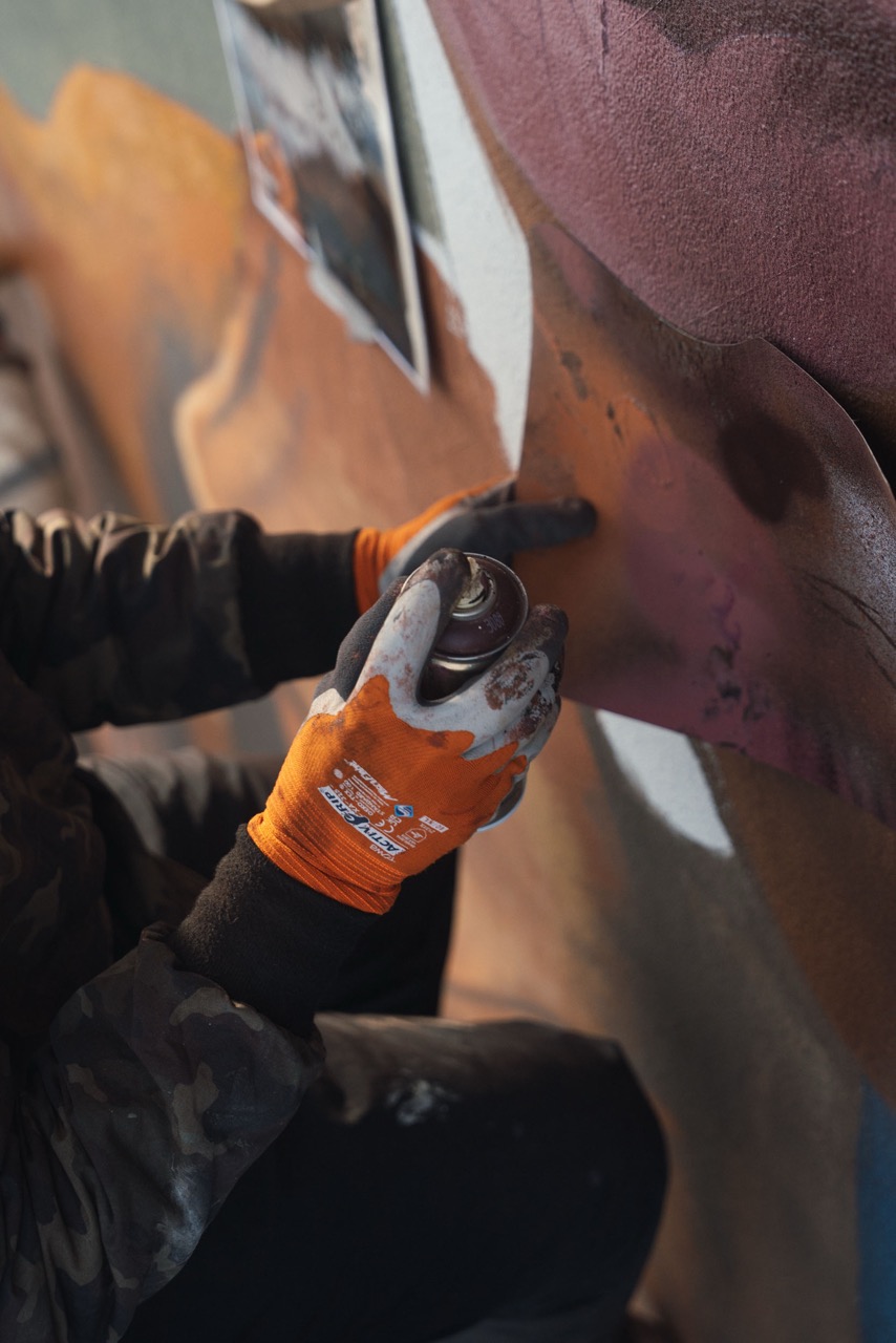 Close-up einer Hand mit Spraydose beim Auftragen dunkler Farbverläufe auf das Ralph-Lauren-Mural.