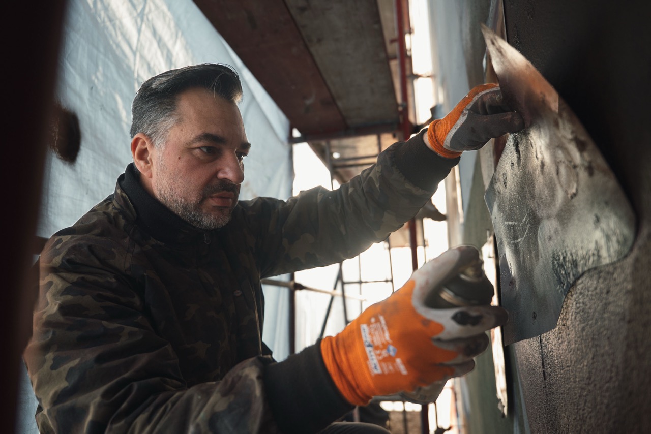Artist arbeitet mit Schablone und Spraydose an fotorealistischen Details eines Ralph-Lauren-Murals in Berlin.
