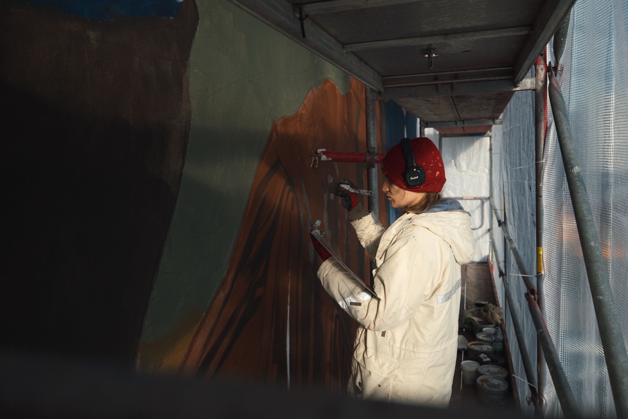 Künstlerin arbeitet mit Spraydose und Schablone an Details eines großformatigen Ralph-Lauren-Murals in Berlin.