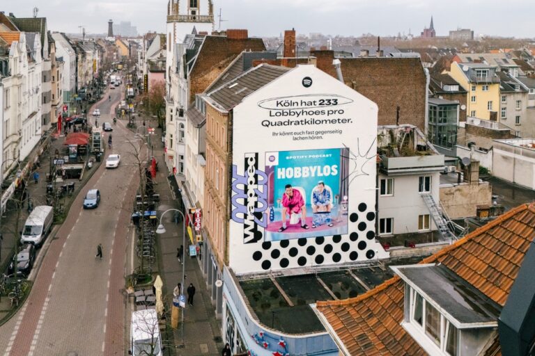 Nächtliche Straßenaufnahme des beleuchteten Spotify Wrapped Murals mit vorbeifahrendem Auto in Köln-Ehrenfeld.