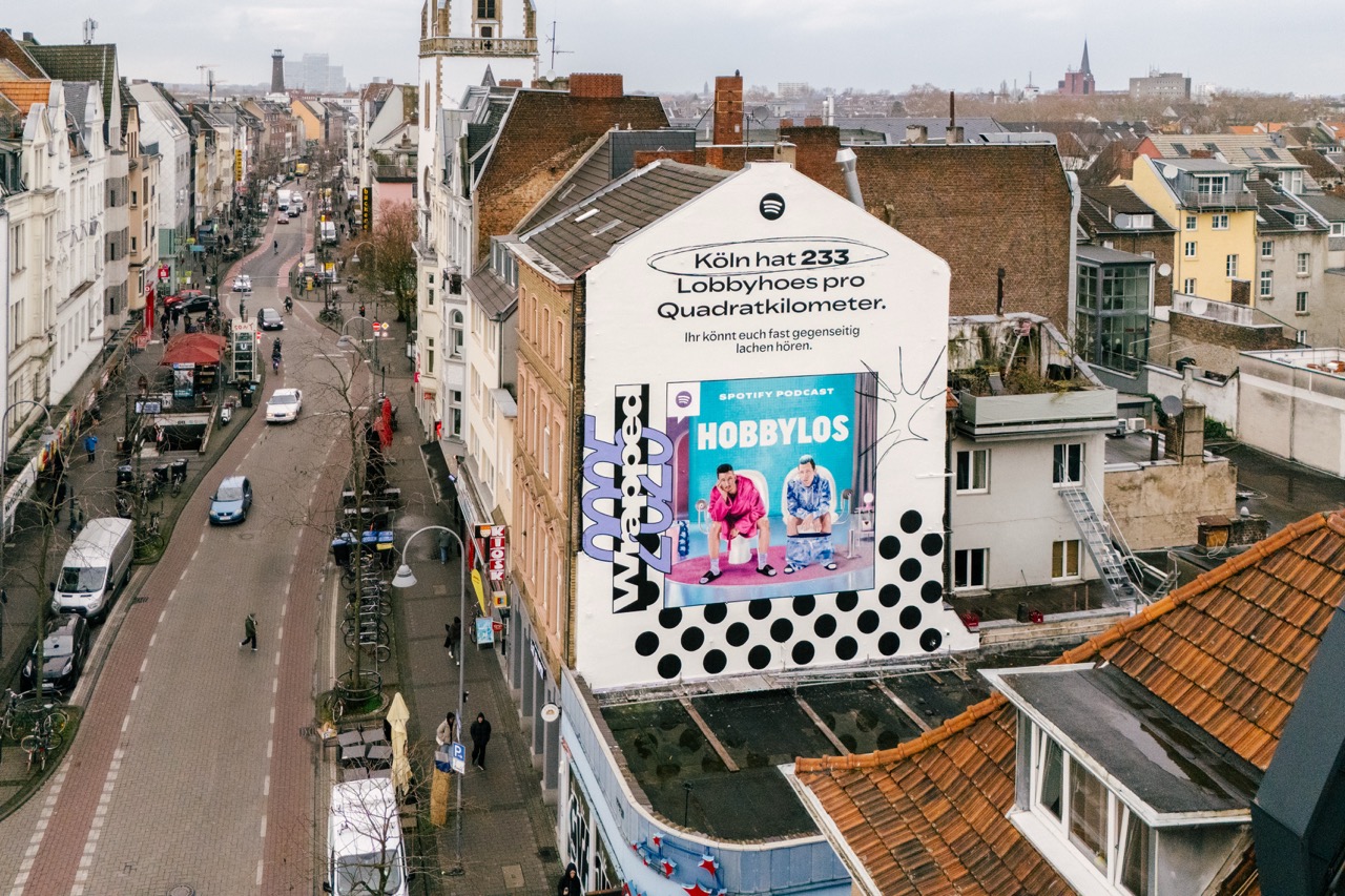 Nächtliche Straßenaufnahme des beleuchteten Spotify Wrapped Murals mit vorbeifahrendem Auto in Köln-Ehrenfeld.