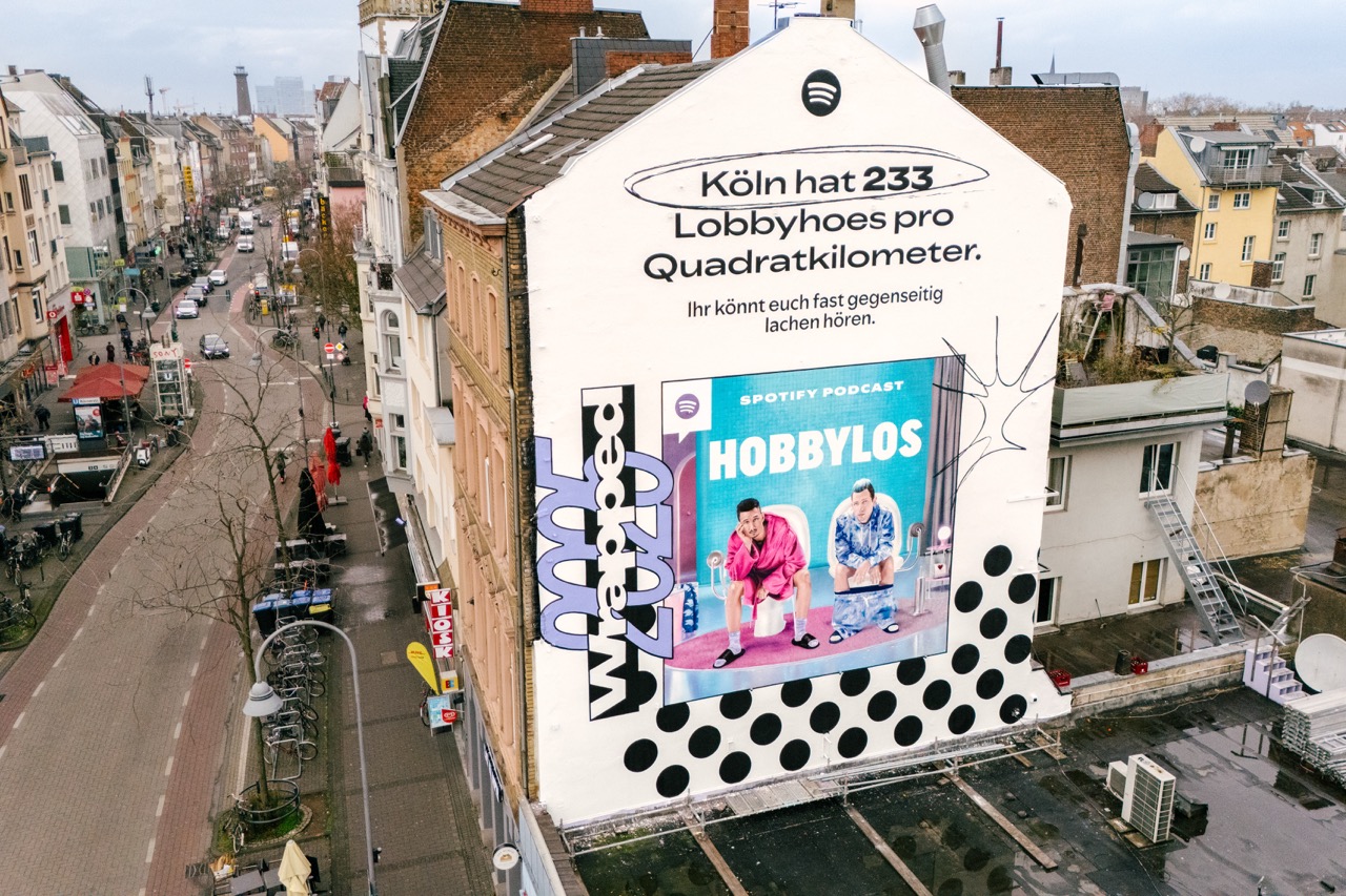 Drohnenaufnahme eines großformatigen Spotify Wrapped Murals mit dem Podcast „Hobbylos“ an einer Hausfassade in Köln.
