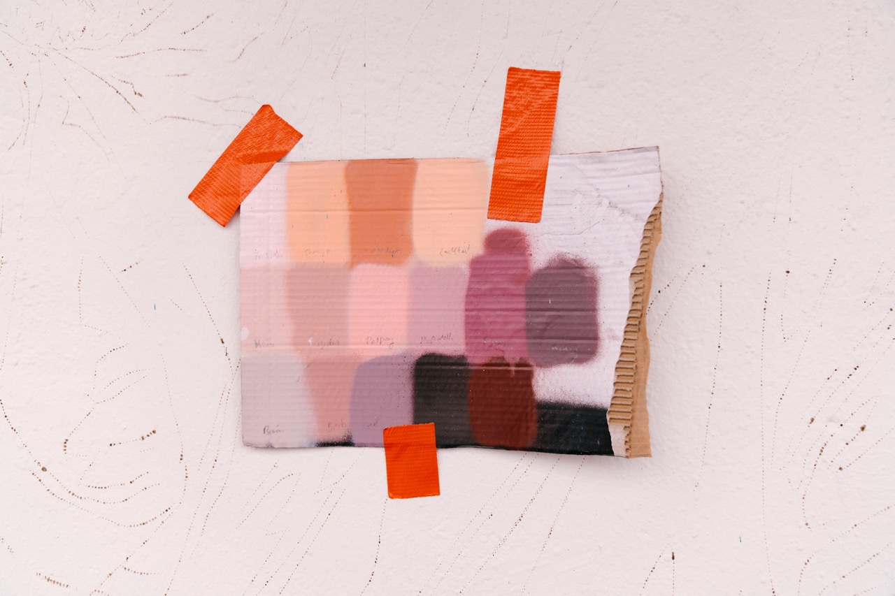 Farbmuster und handbeschriftete Farbreferenzen sind mit orangem Tape an einer Wand befestigt.