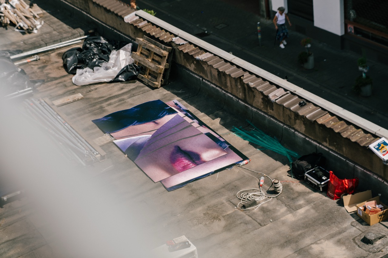 Großformatig bedruckte Motivplatten mit dem Gesicht von Wednesday liegen vorbereitet auf dem Dach für die spätere Montage an der Fassade.